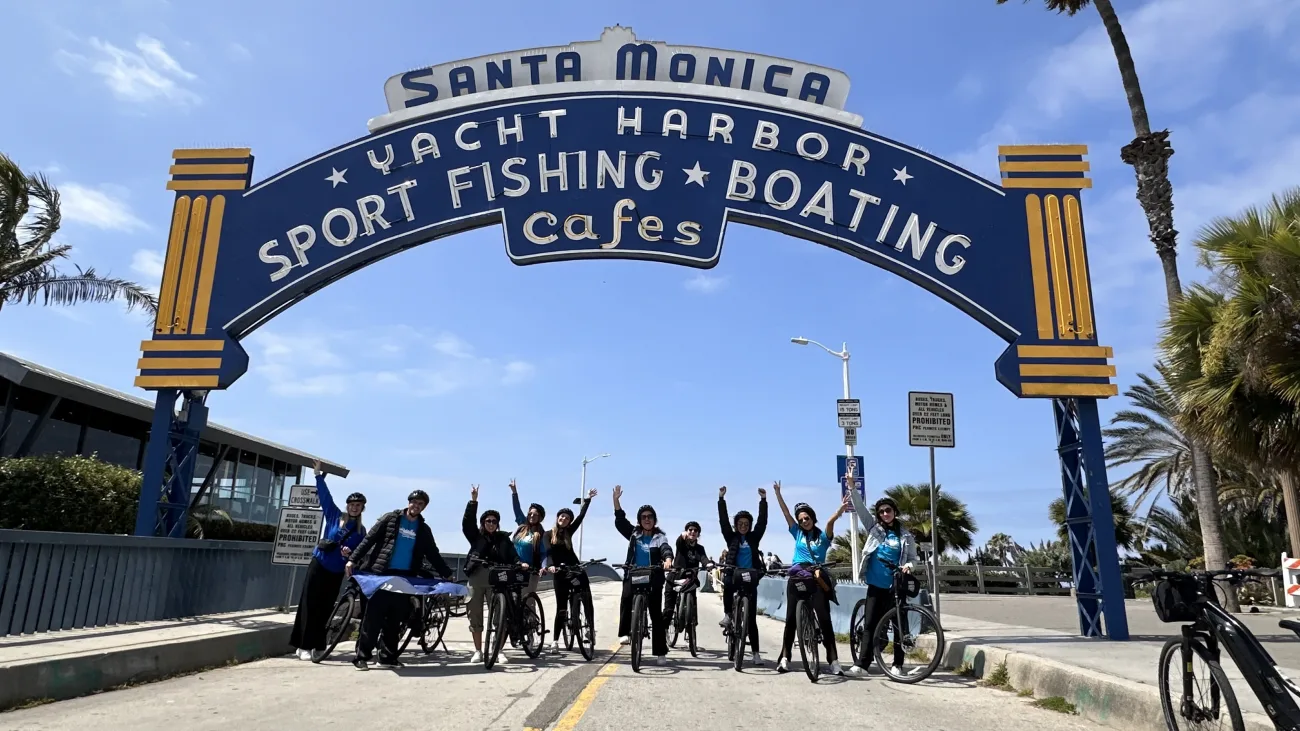 Guests throw their arms up and pose under the entrance to the Santa Monica Pier.