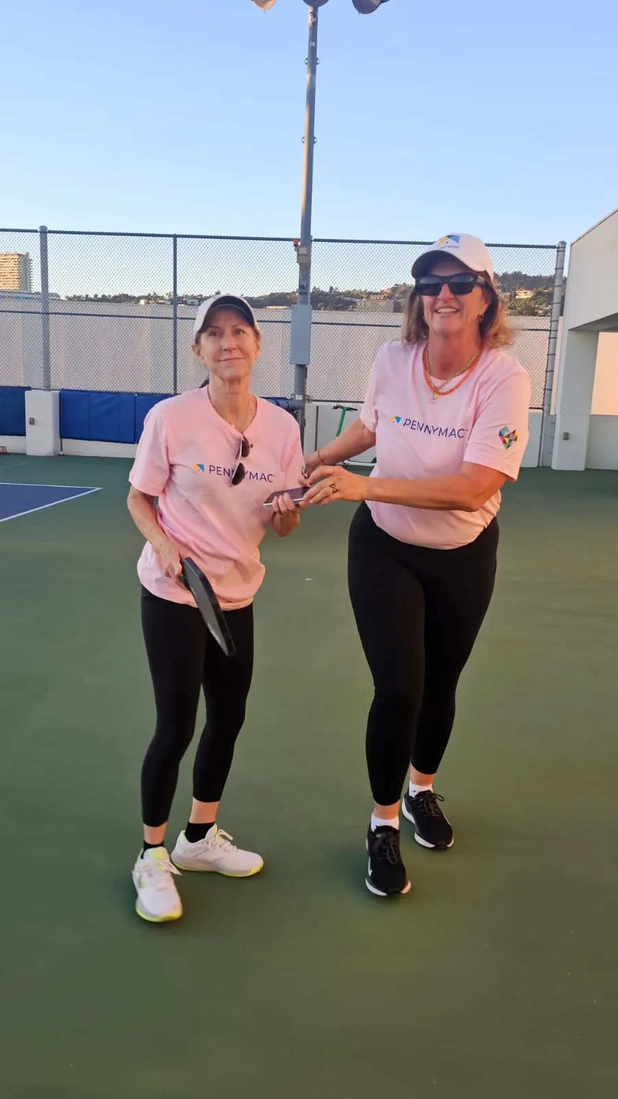 two women in pink corporate shirts pose with pickleball rackets