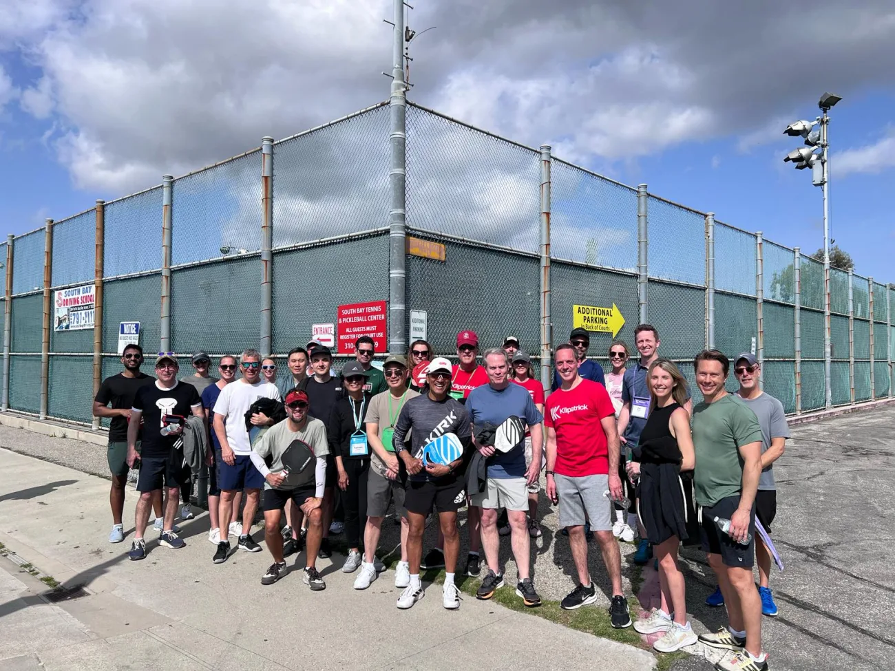 A large corporate group poses outside a pickleball court