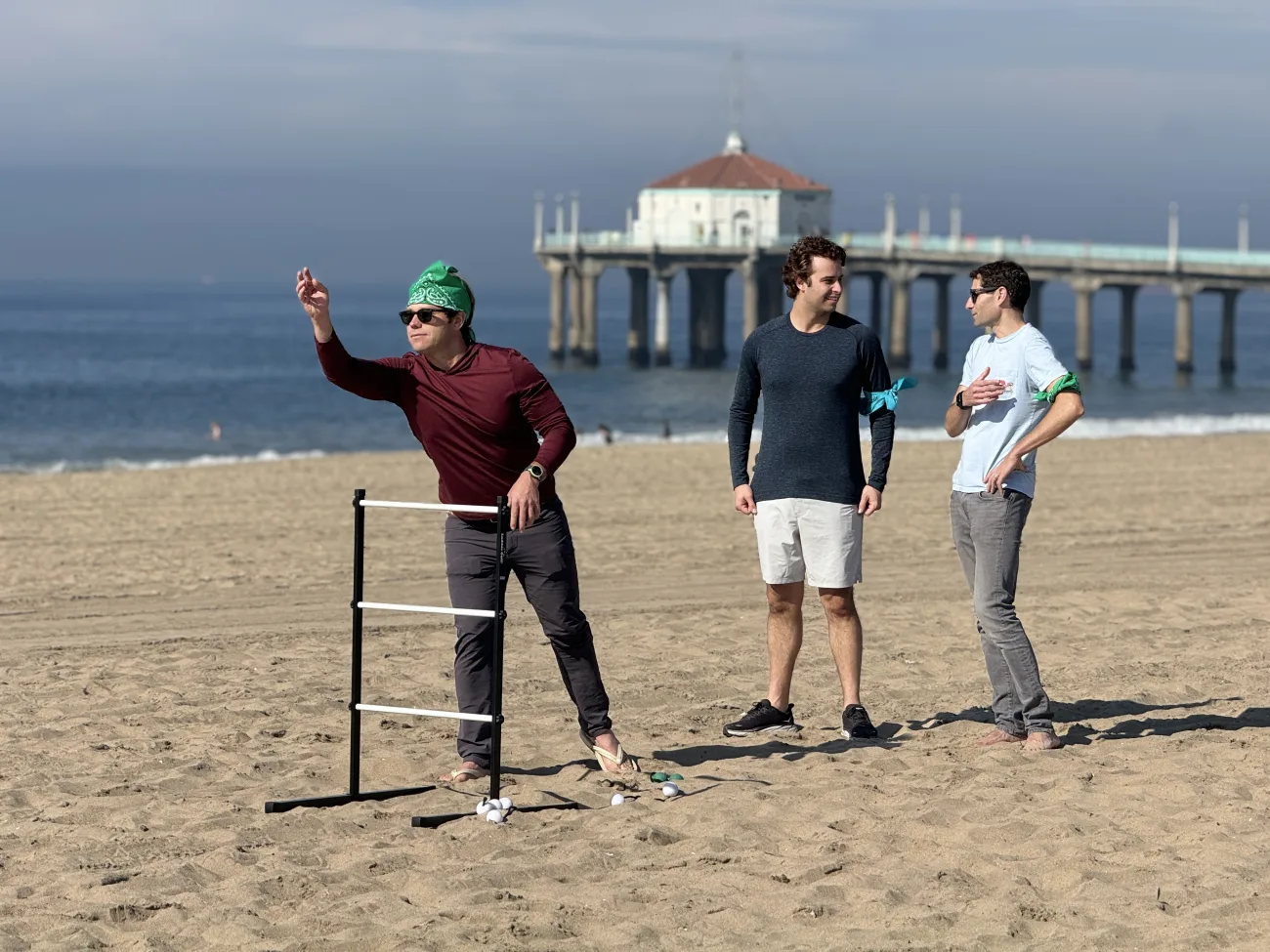 A group of men playing cornhole with the pier in the background