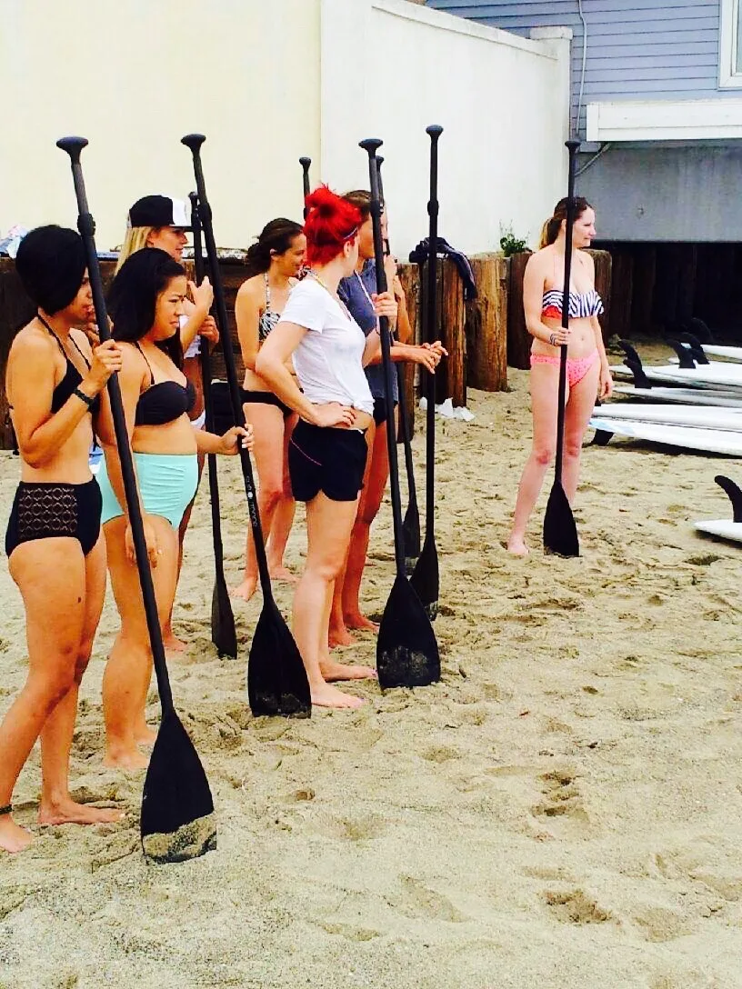 Guests stand on the sand with paddles learning how to operate the paddle board.