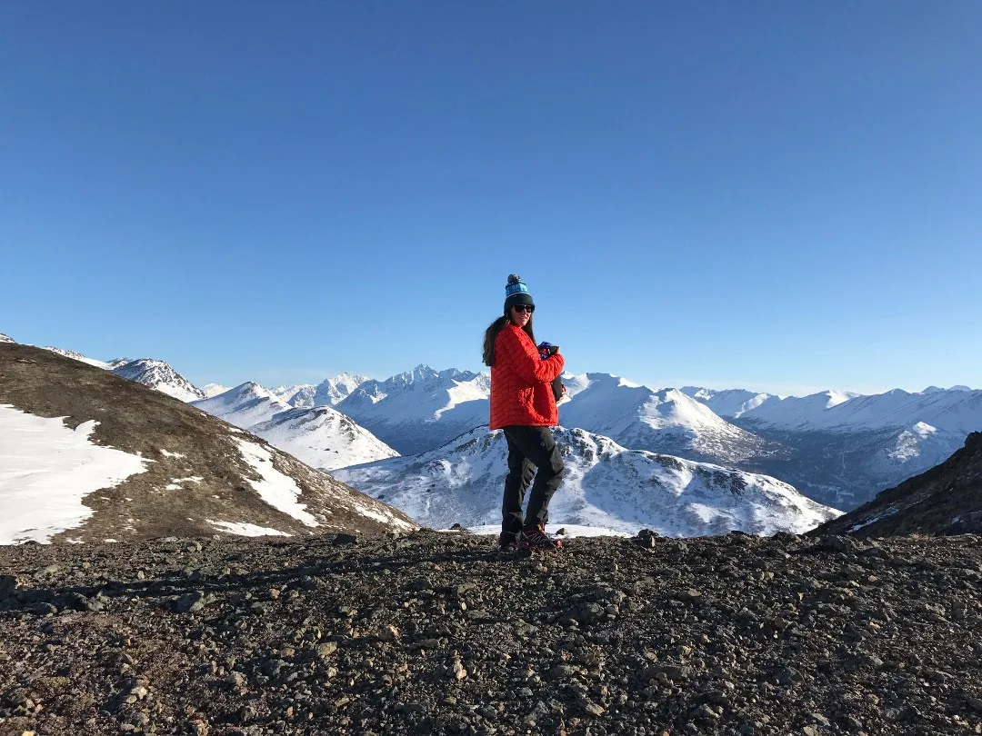A woman poses at the top of a snowy mountain