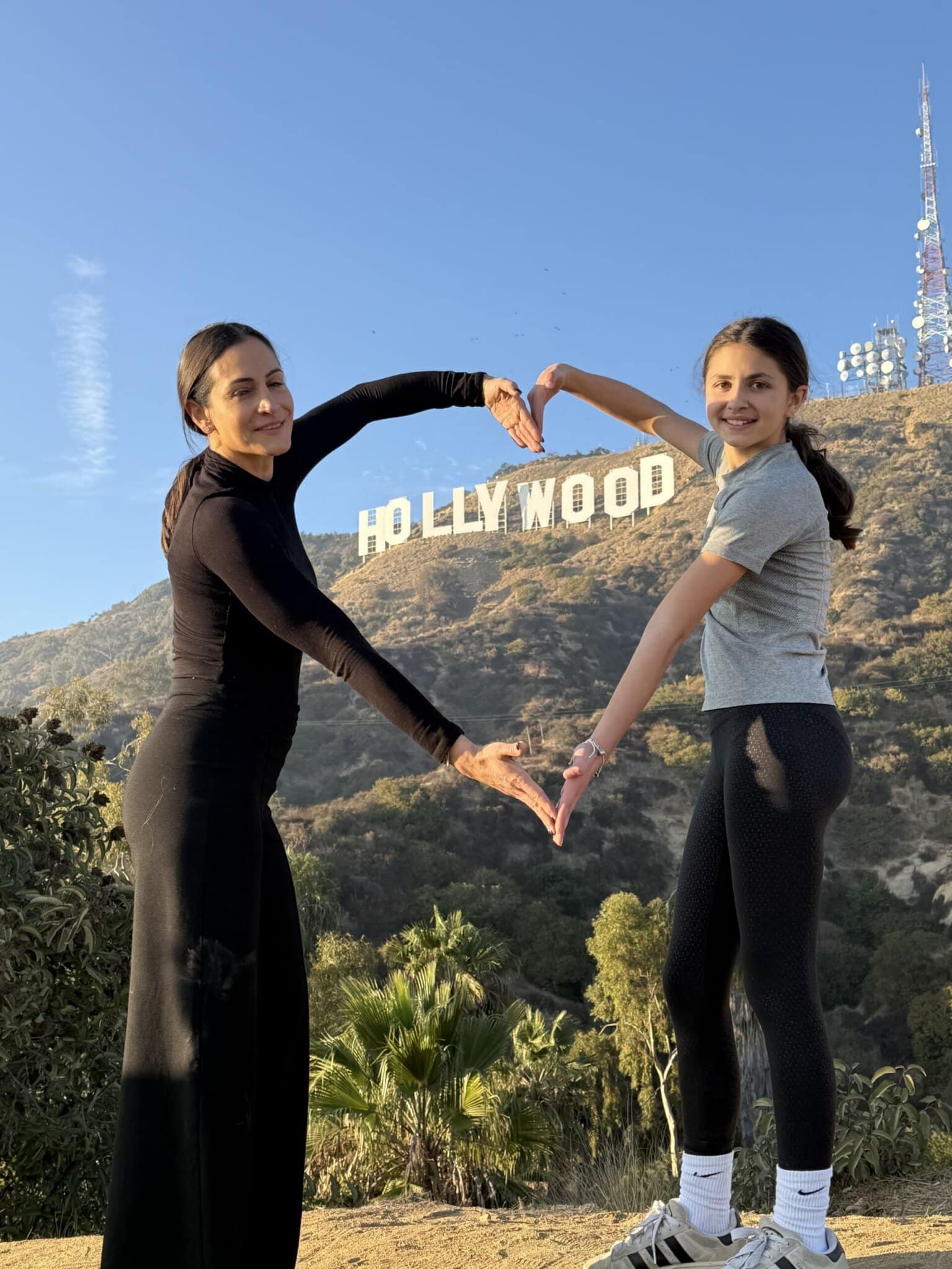A mother and daughter make a heart around the Hollywood Sign