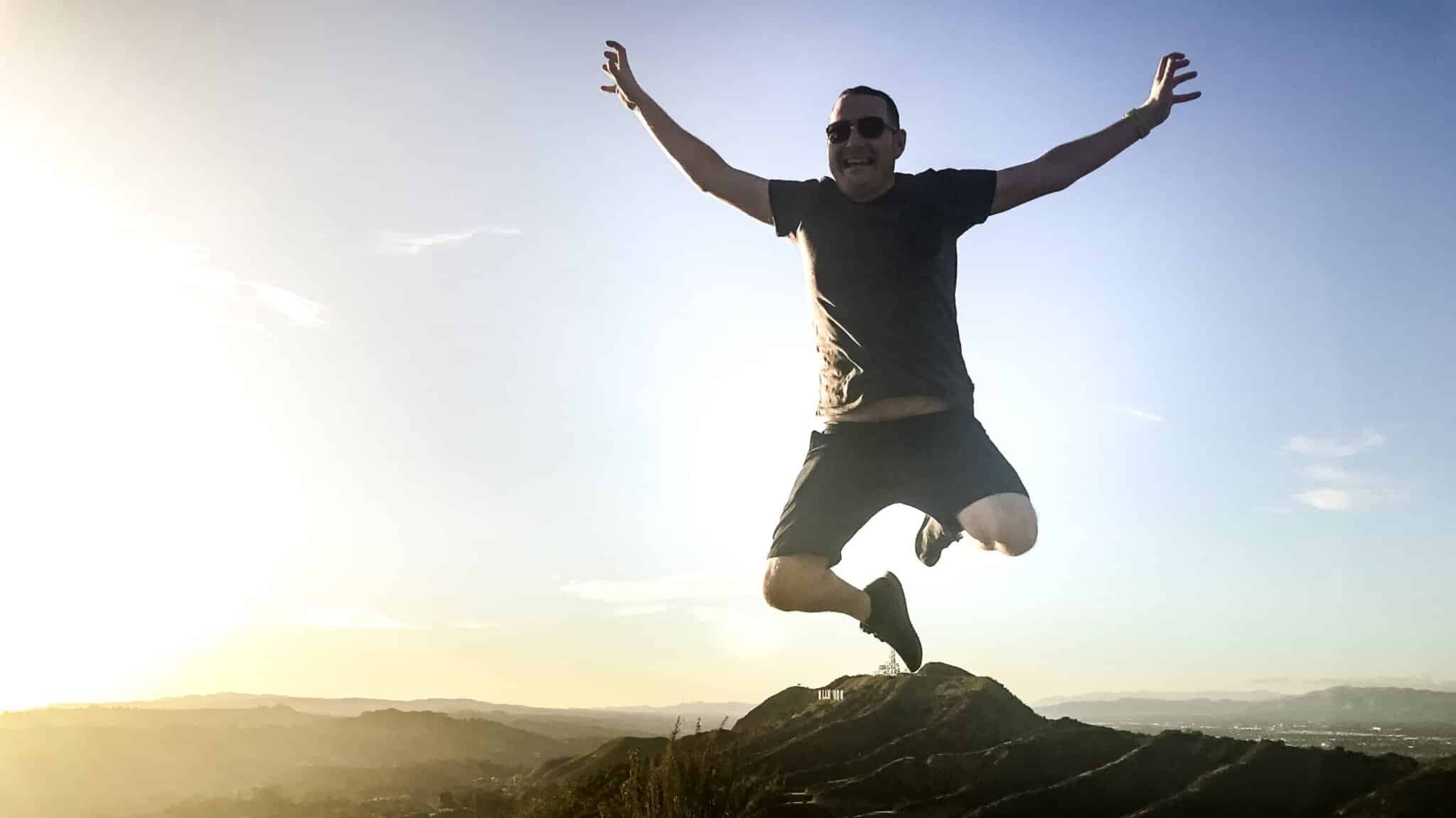 A man jumps over the Hollywood Sign in the distance on the Griffith Observatory Hike