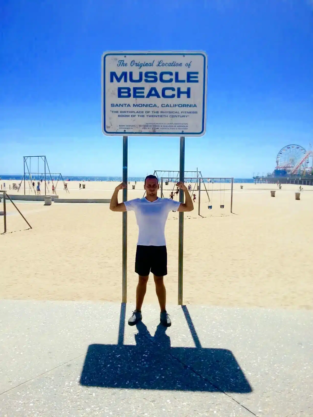 A guest poses with the muscle beach sign in Santa Monica