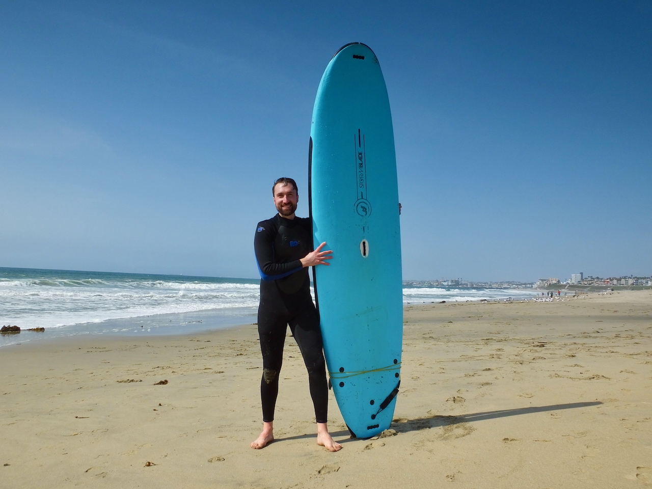 A guest poses with their surfboard during a group surf lesson