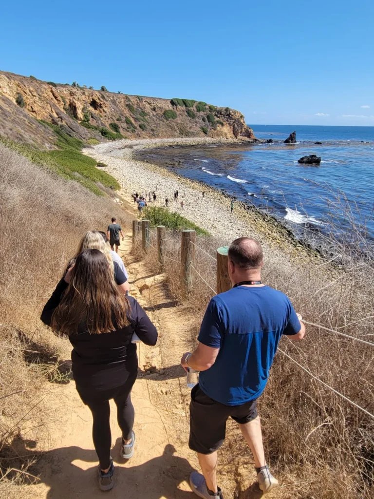 Group hiking down a coastal trail toward the beach during a guided Palos Verdes nature walk near Terranea Resort