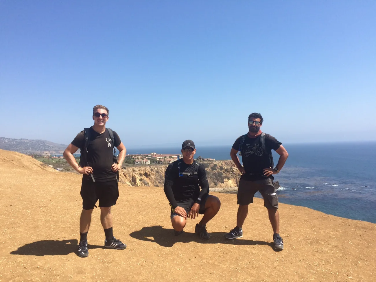 Three hikers posing on a scenic cliffside during a guided hike in Rancho Palos Verdes, with expansive ocean views and rugged coastline in the background.