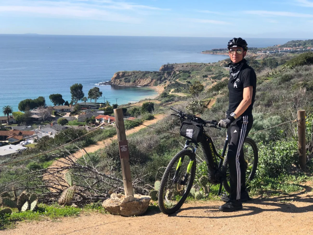 A man stands above a stunning view of the pacific coast on a trail with his bike on the palos verdes peninsula.