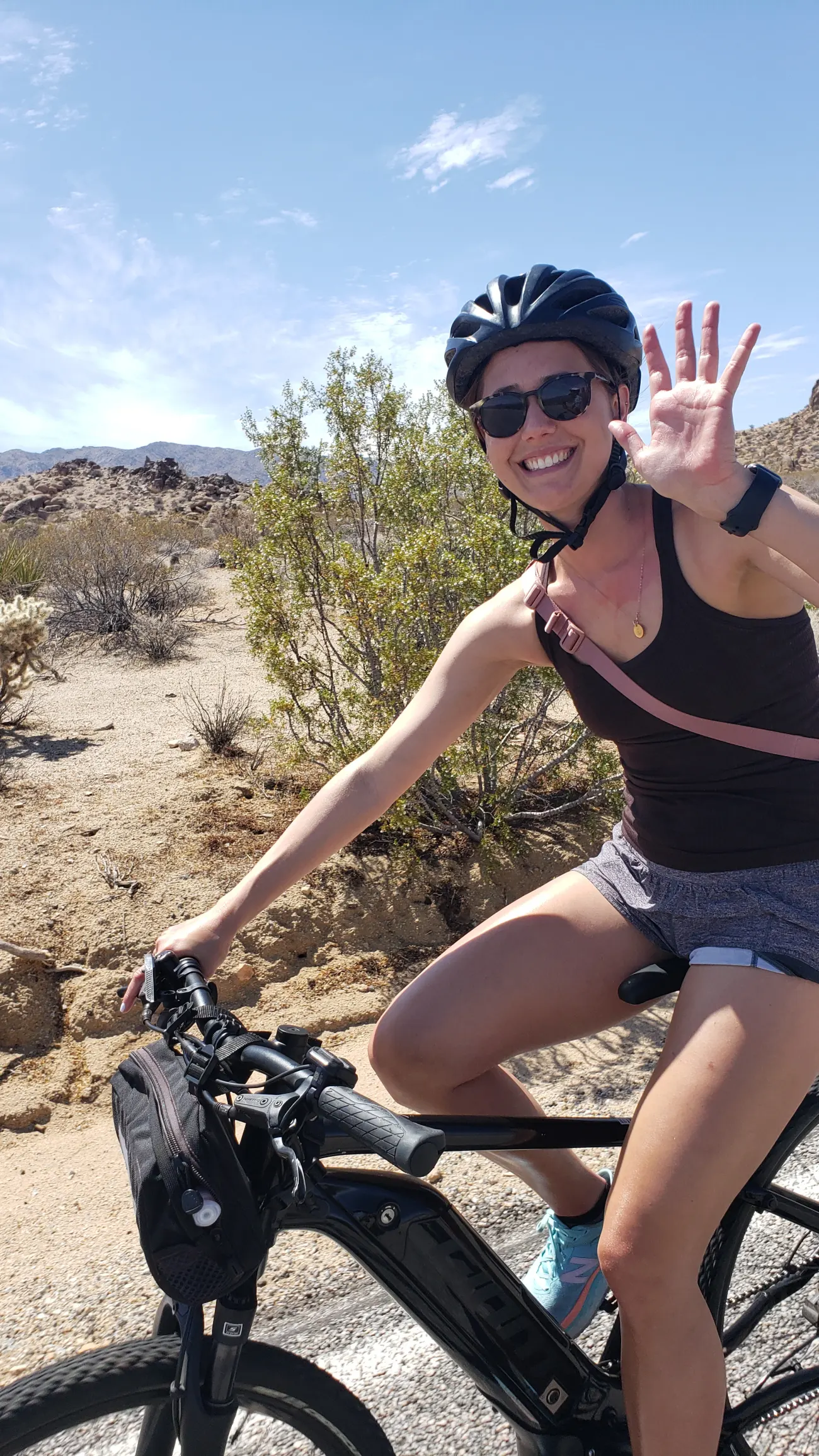 A woman waves and smiles on a bike in Joshua Tree National Park