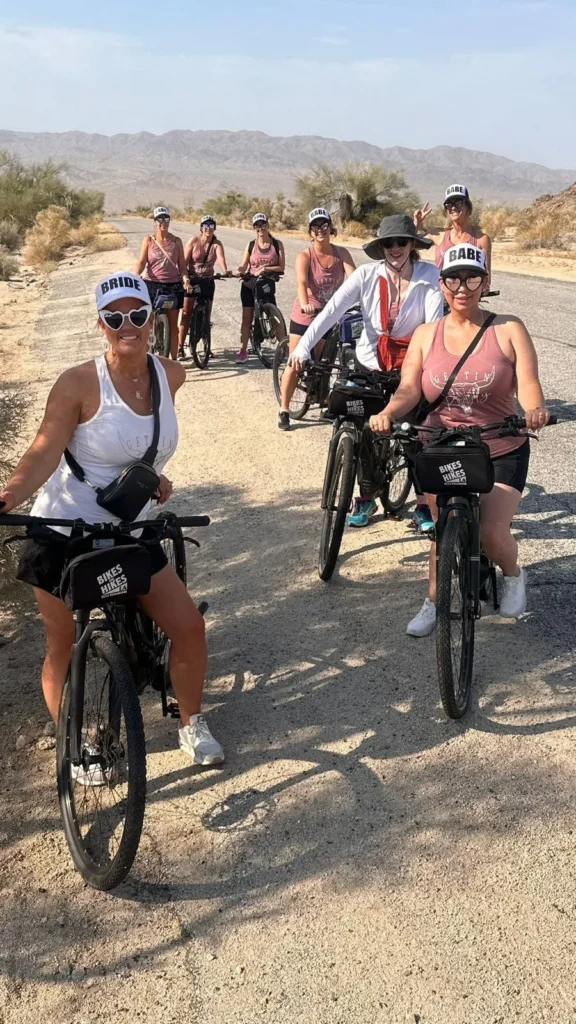 Several women on bikes smile on bikes on a desert road in Joshua Tree