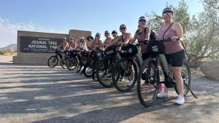 Riders on the Joshua Tree Bike Tour pose in front of the Joshua Tree sign