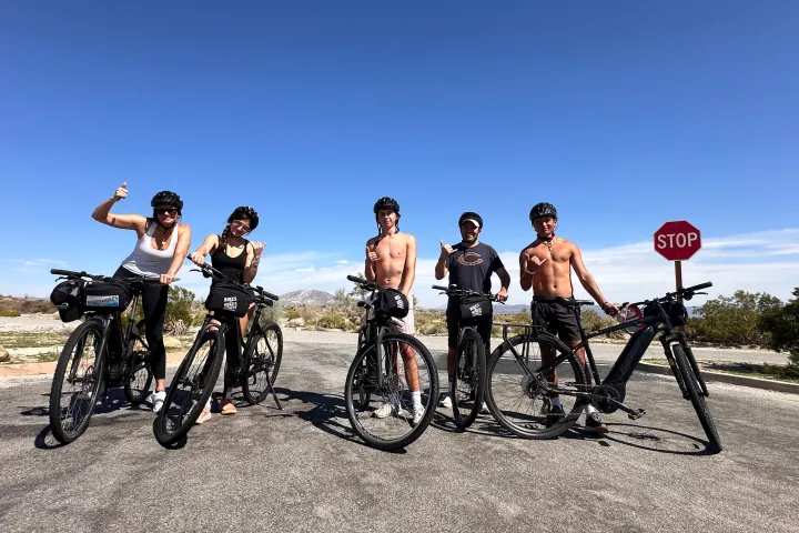 A group of riders pose on a desert road with bikes in Joshua Tree National Park