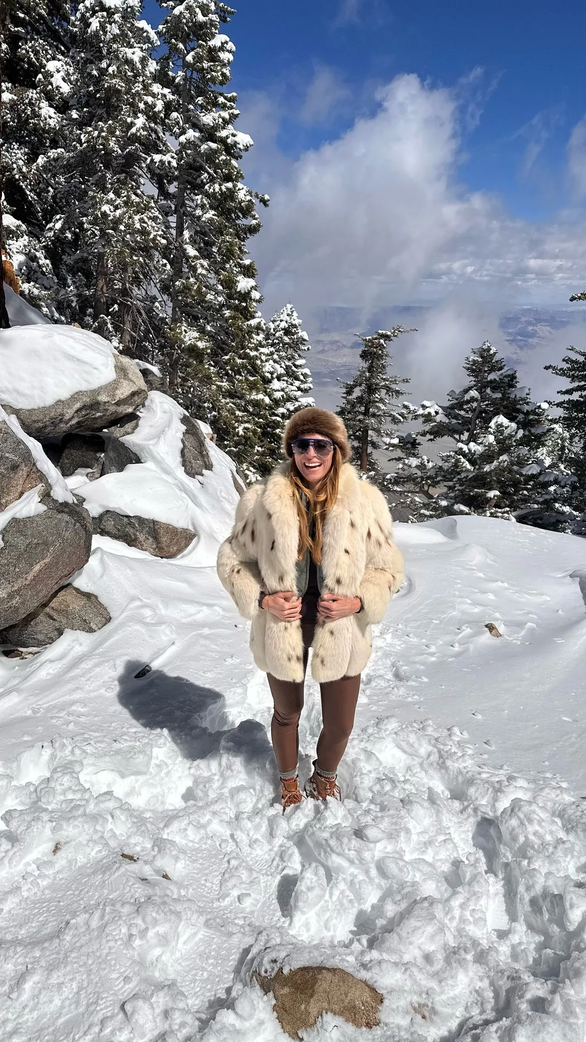 A guest smiles in a big jacket on top of Mt. Jacinto