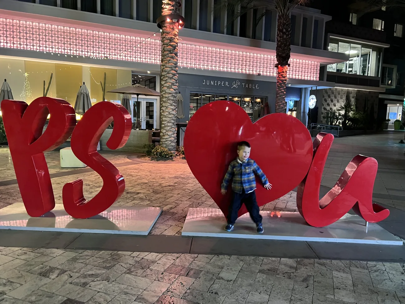A little boy stands with a "PS loves u" sign