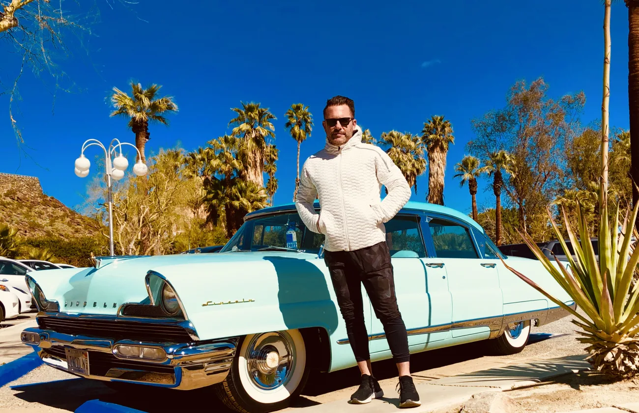 A guest stands with a cool older car in palm springs
