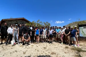 A group of hiking guests stand in the middle of the joshua tree desert and pose with structures in the background.