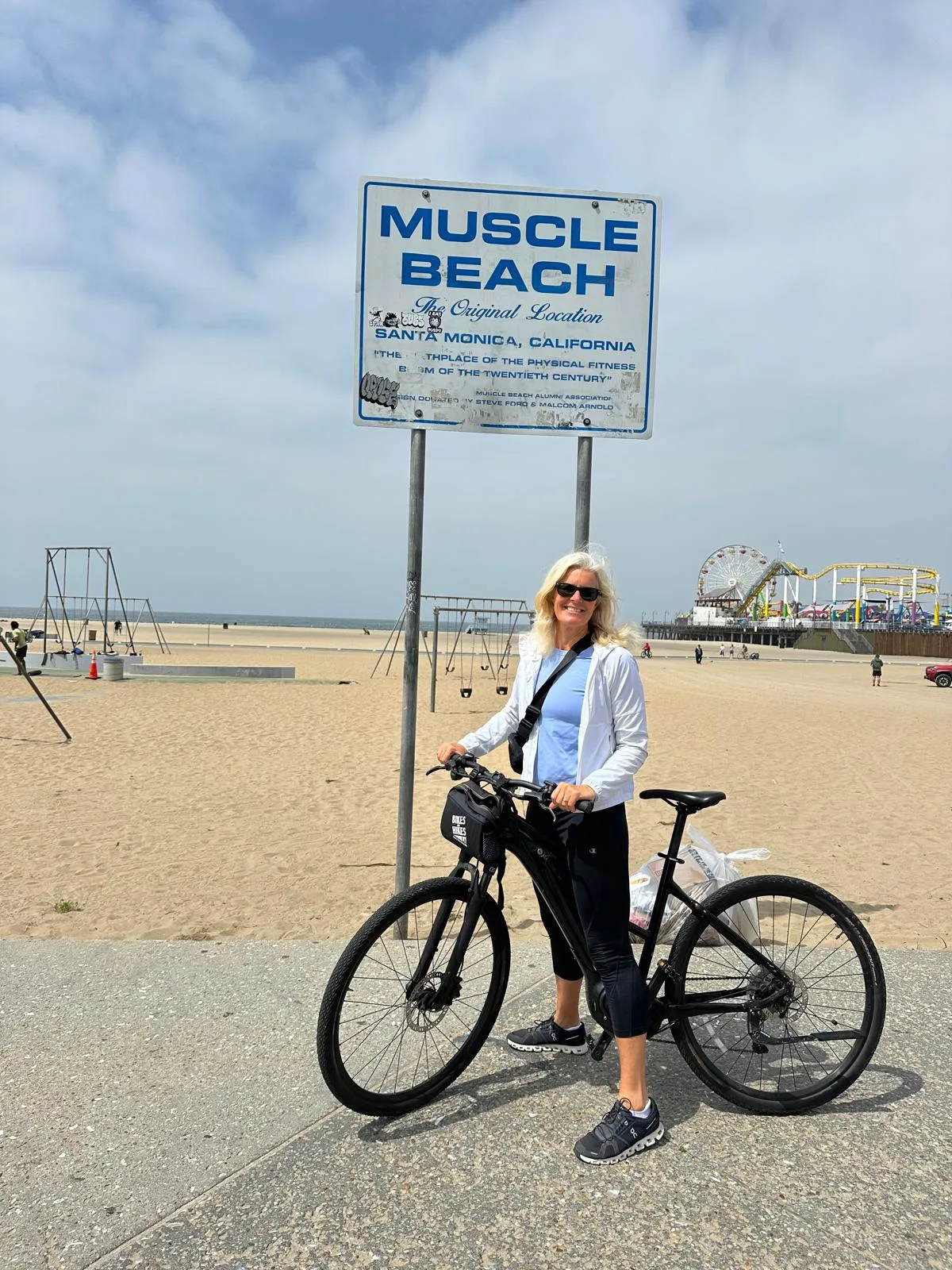 A woman on a bike poses with the Muscle Beach sign in Santa monica