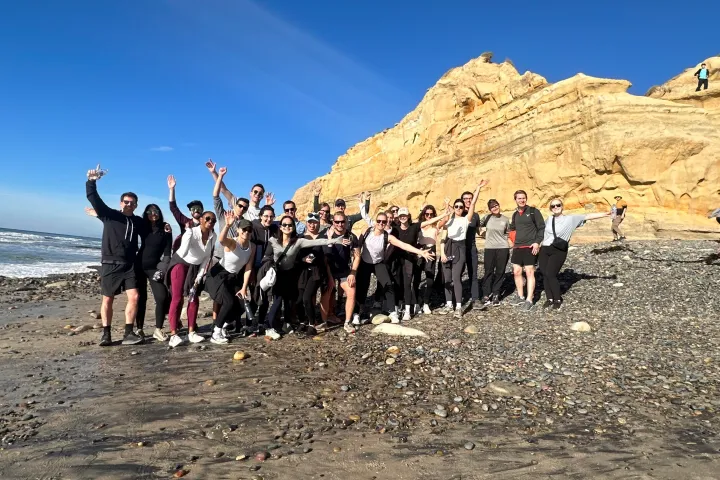 guests stand on a beach on San Diego with their arms up after a hike in Torrey Pines