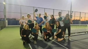 a group poses on a pickleball court with their rackets