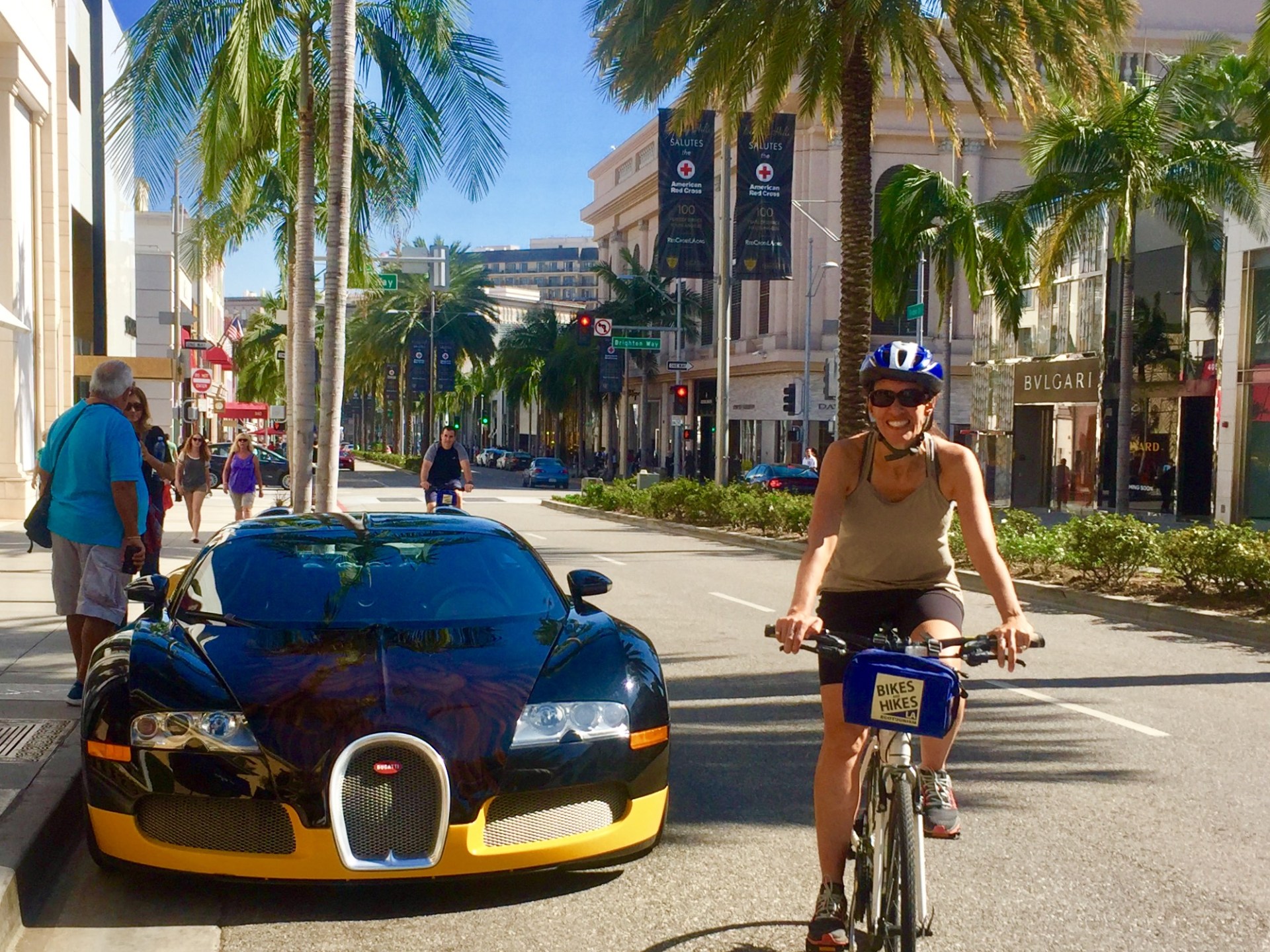 a group of people riding bikes down a street next to a luxury car beverly hills