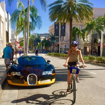 a group of people riding bikes down a street next to a luxury car beverly hills