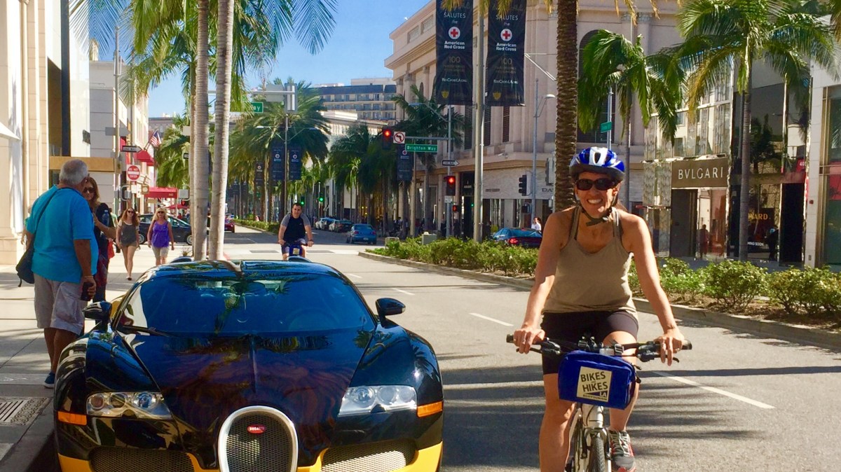 a group of people riding bikes down a street next to a luxury car beverly hills
