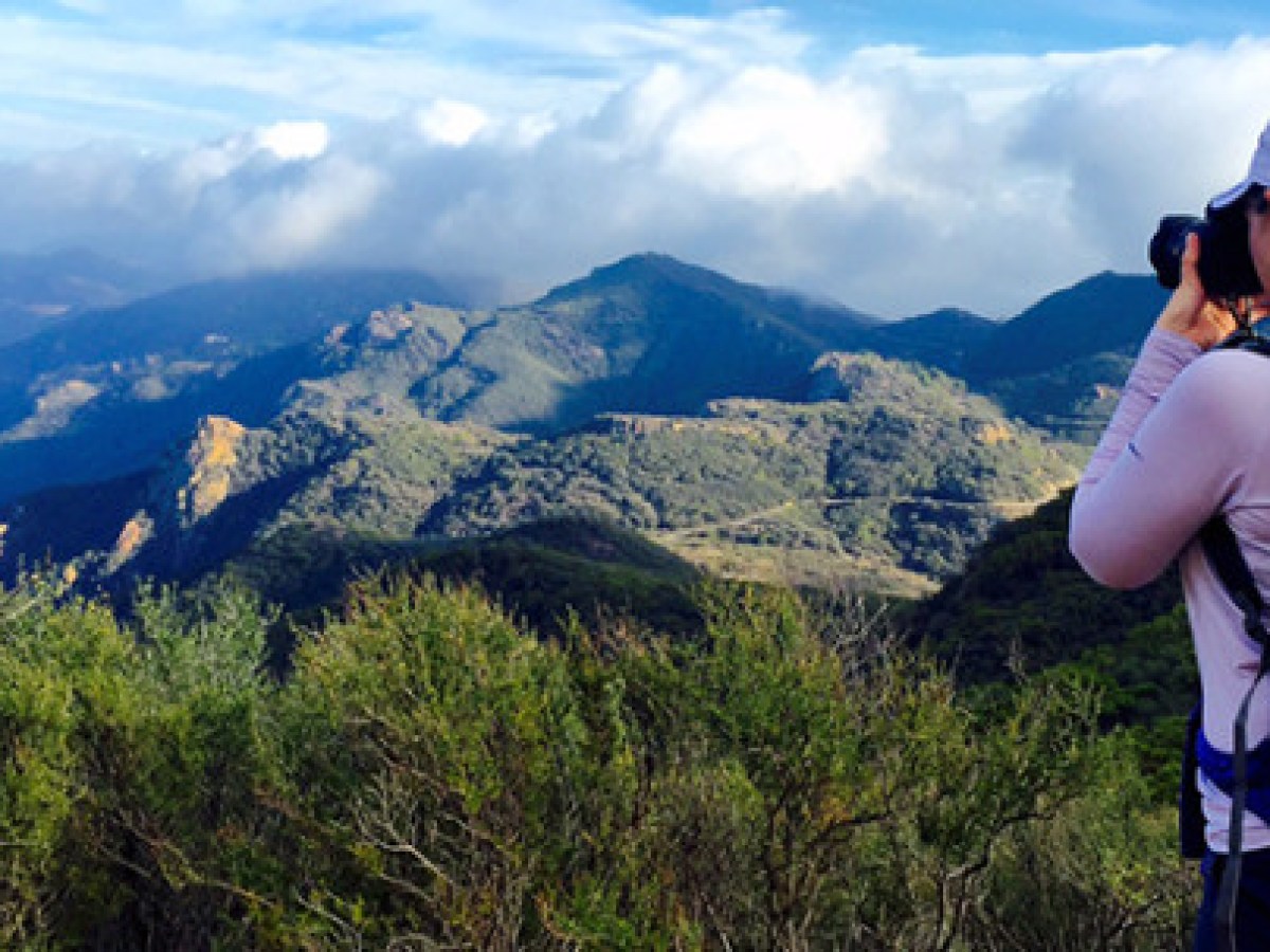 A woman taking a picture of Malibu canyon with a large canyon