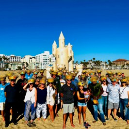 a group of people standing in front of a crowd posing for the camera in front of a sand castle doing group team building in los angeles