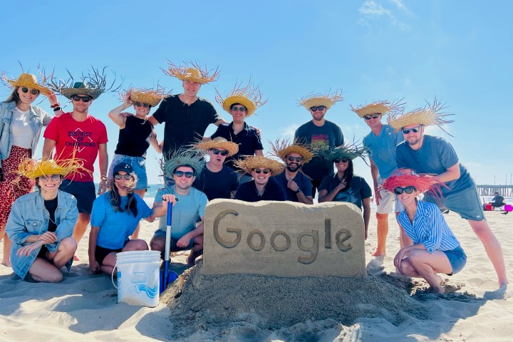 a group of people posing for a picture behind a sand castle that says google