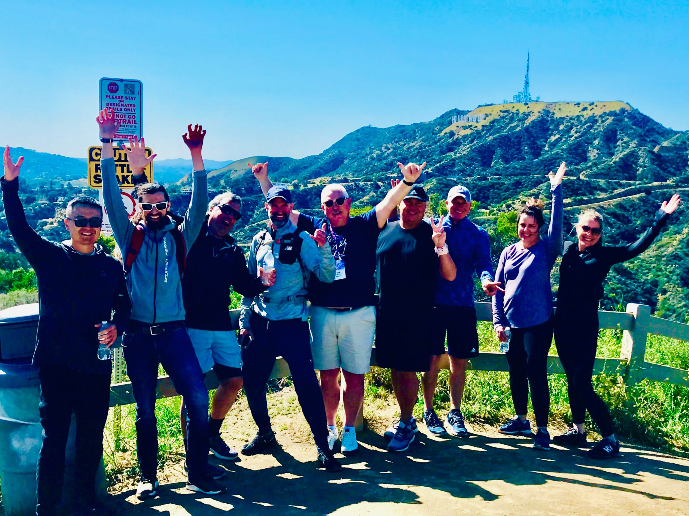 a group of people standing in front of the hollywood sign on a team building tour