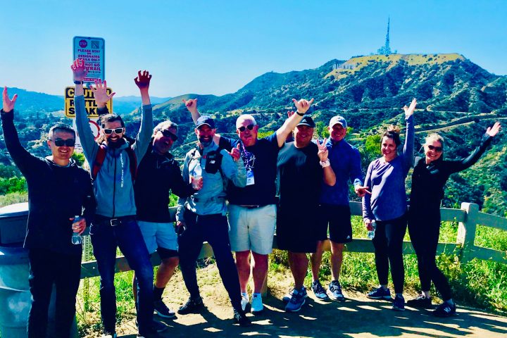 a group of people standing in front of the hollywood sign on a team building tour