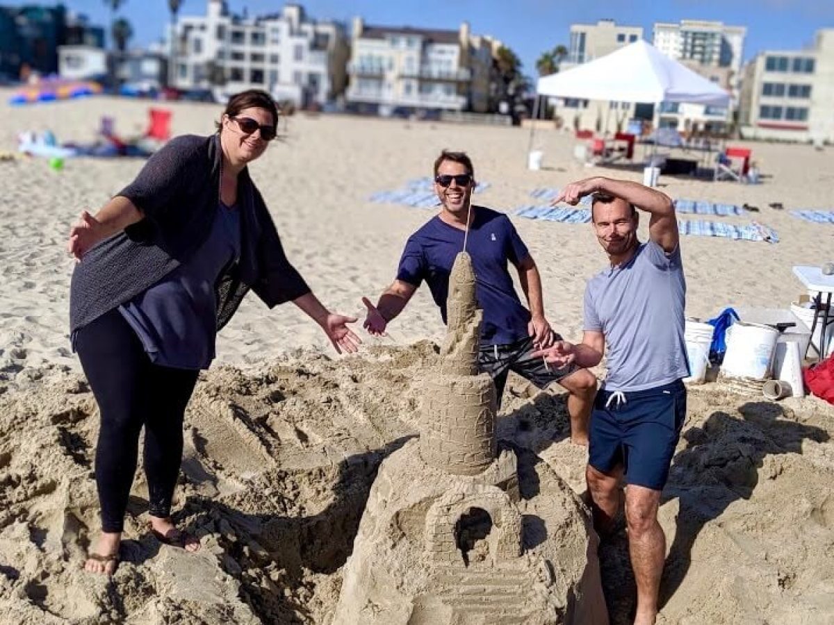 Three people posing with their sandcastle