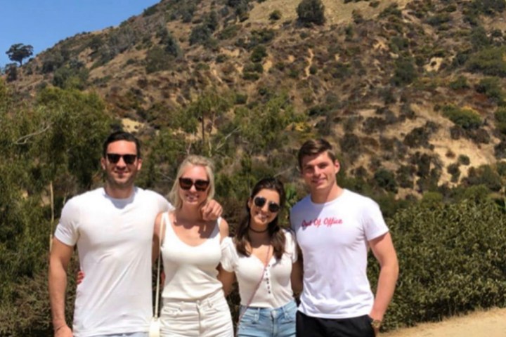 four people stand below the hollywood sign