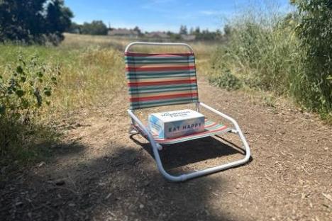 a folding chair with a boxed lunch on a dirt path