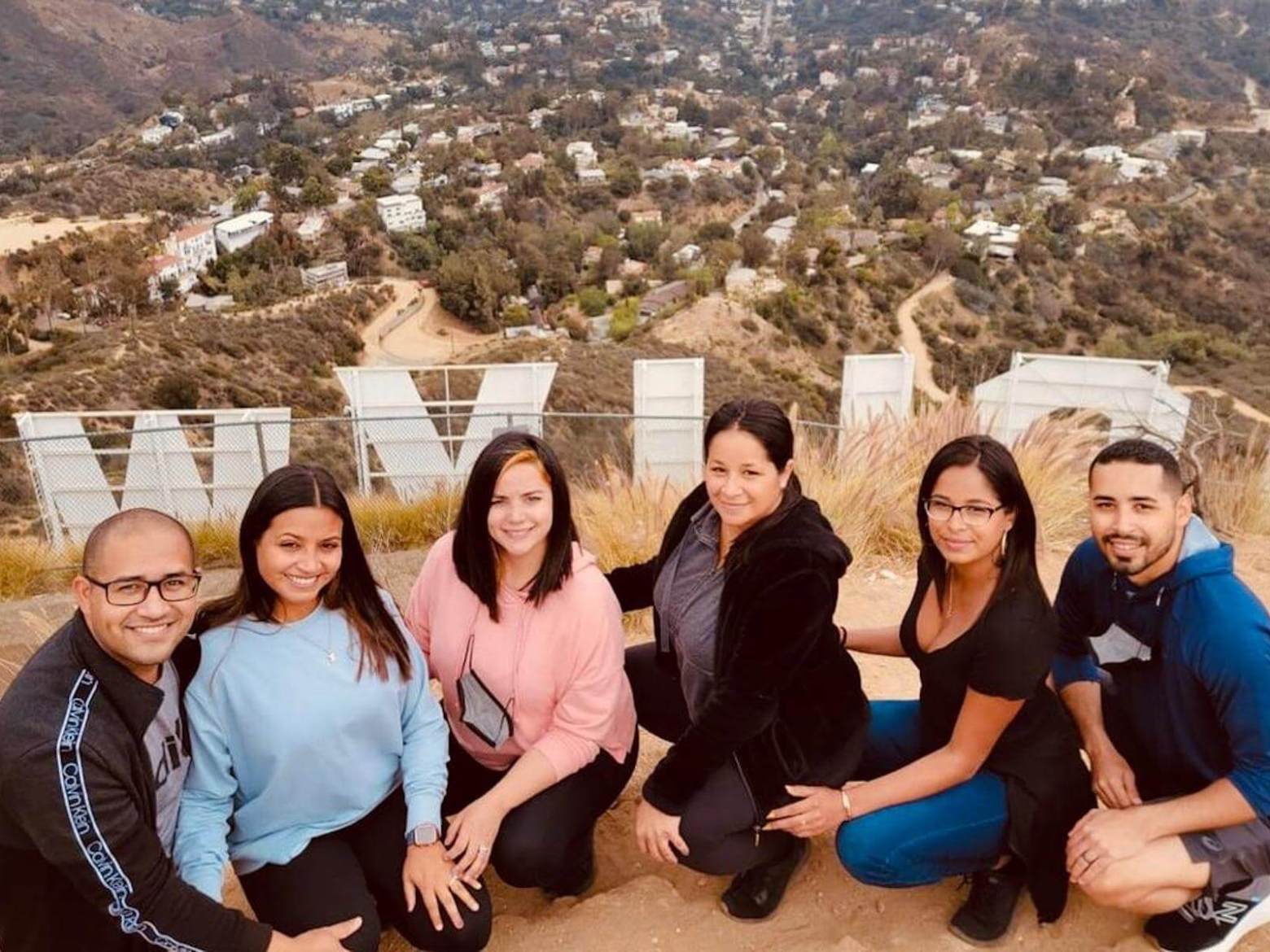 a group of people posing on a hike behind the hollywood sign