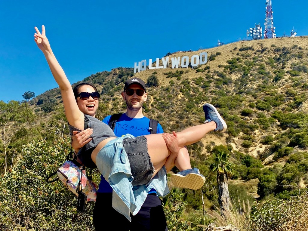 two people taking a hollywood sign tour in los angeles in front of the hollywood sign