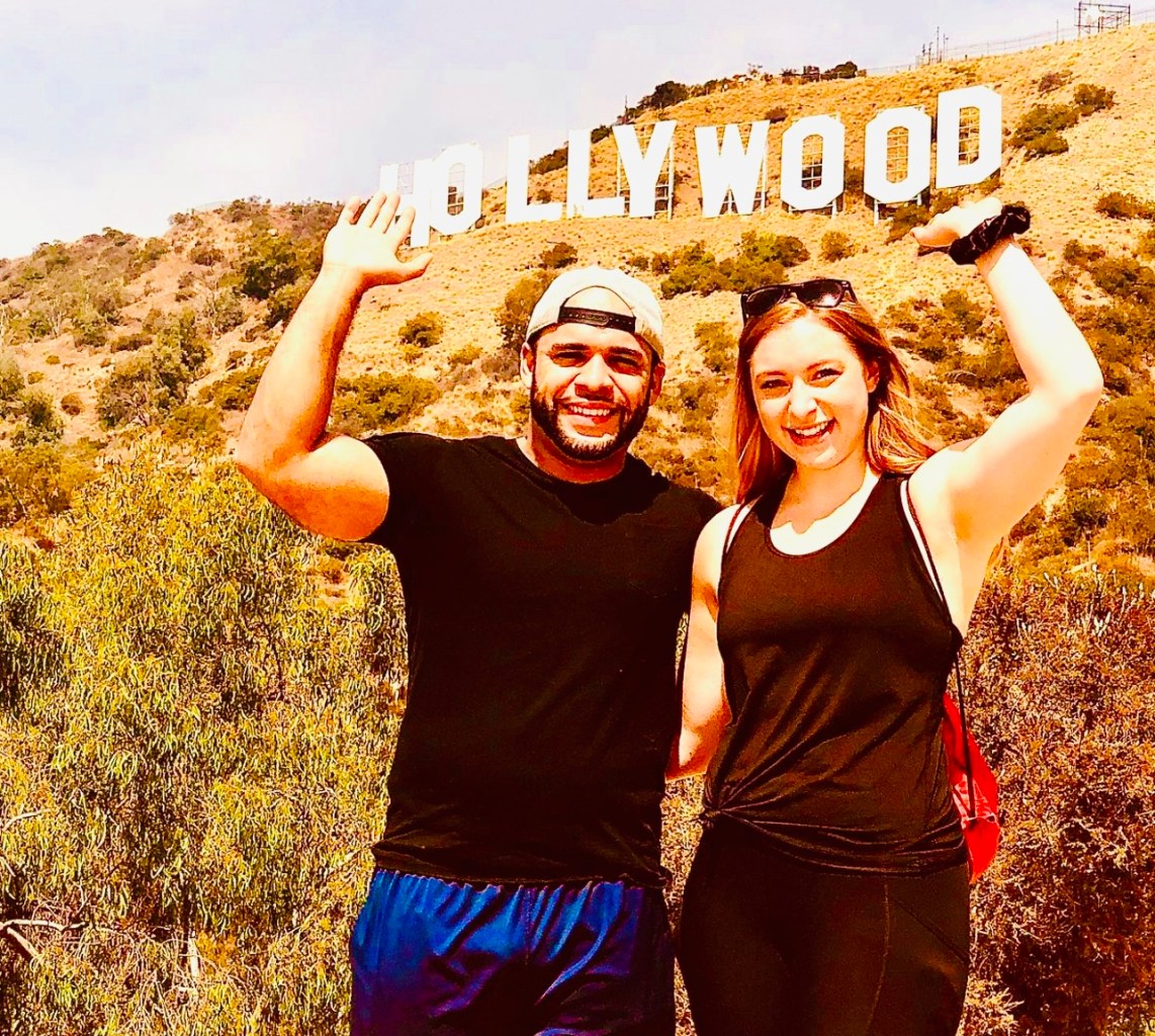 two people standing below the hollywood sign