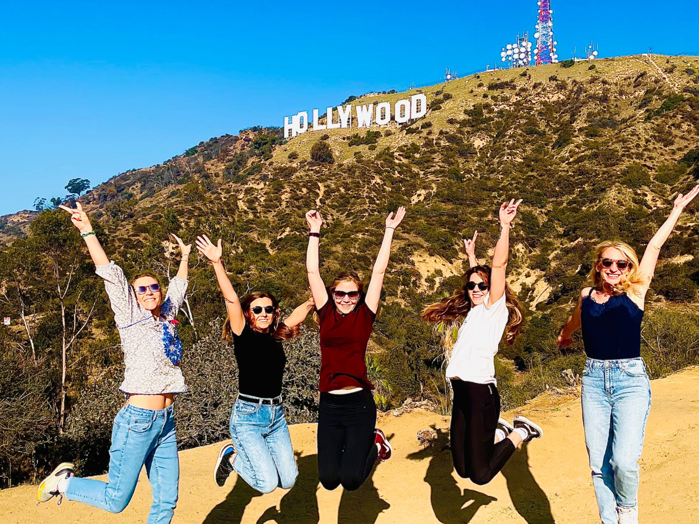 5 people jump into the air below the hollywood sign