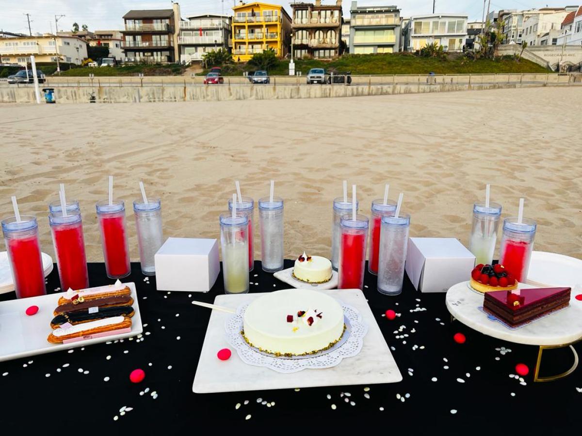 an assortment of desserts and festive drinks on top of a table on a beach