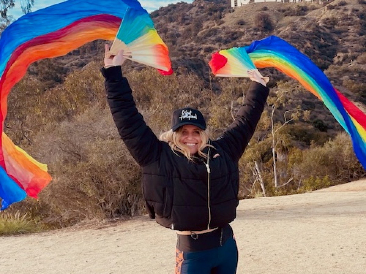 a person waving two rainbow flags under the hollywood sign