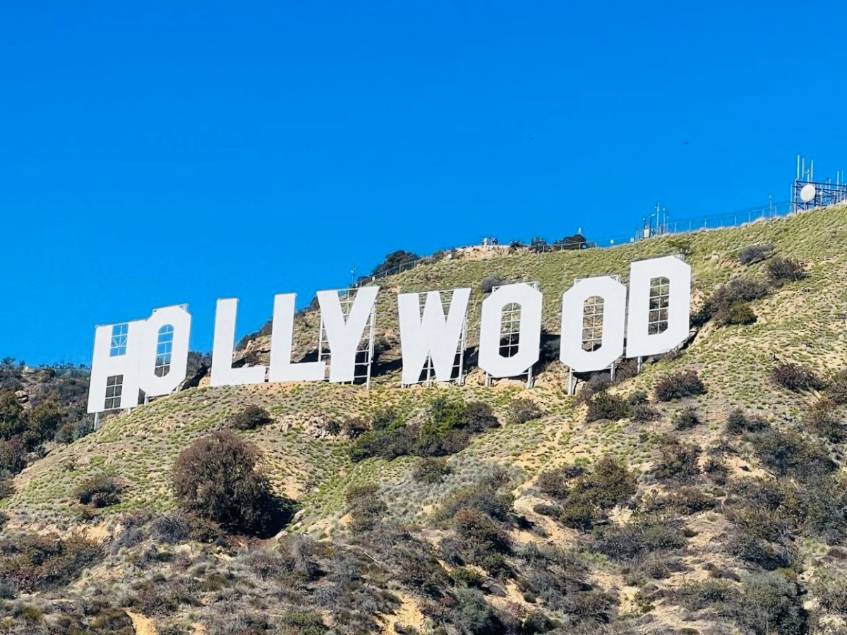 a sign on the side of a hill with Hollywood Sign in the background