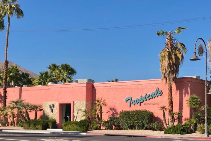 a street lined with palm trees and a building in the background