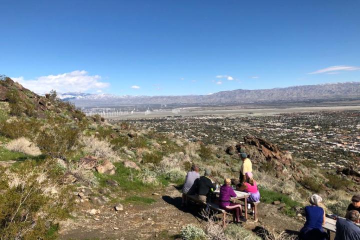 a group of people sitting on a mountain overlooking palm springs on a palm springs hike