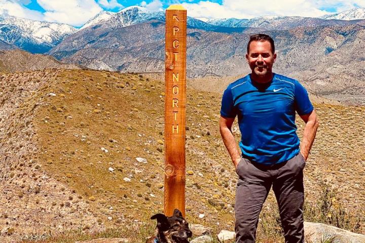 a man and a dog next to a wooden signpost in the mountains
