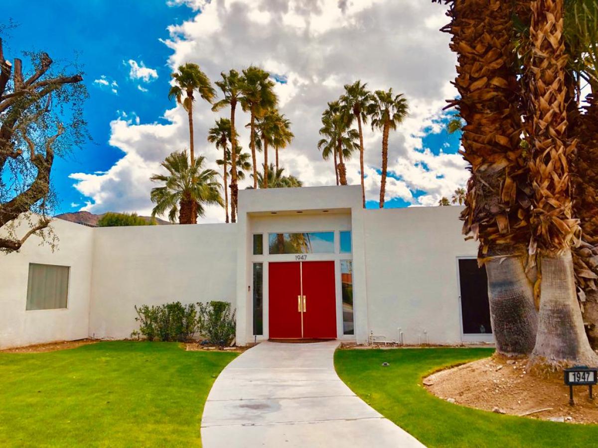 a pair of red doors on a white house in front of a row of palm trees