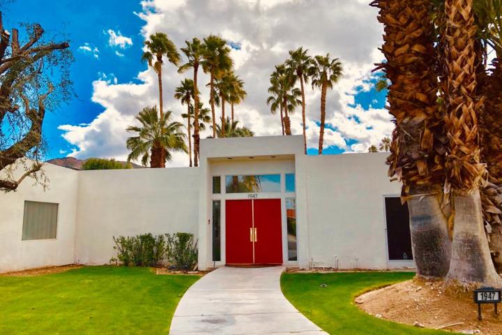 a pair of red doors on a white house in front of a row of palm trees