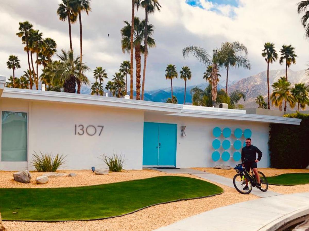 a person on a palm springs bike tour next to a white and blue house and some palm trees