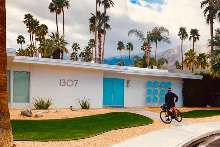 a person on a palm springs bike tour next to a white and blue house and some palm trees