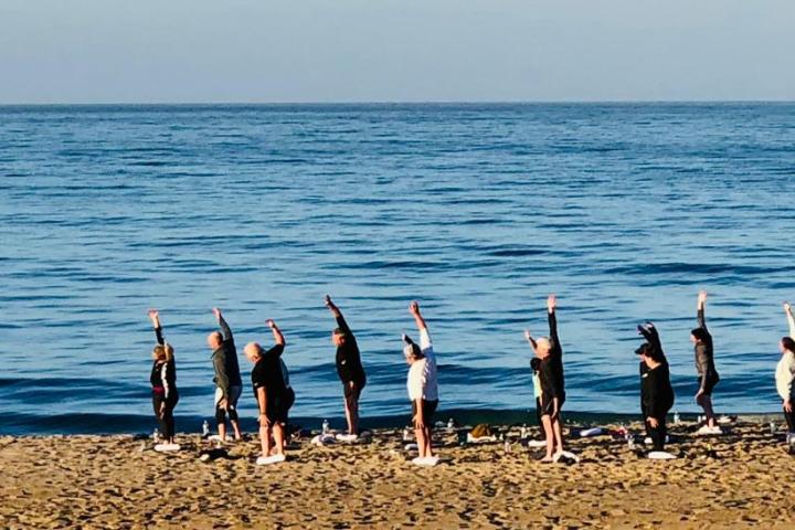 a group of people doing group yoga by the ocean